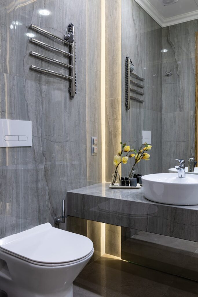 Interior of modern bathroom with sink placed at mirror on marble gray surface with flowers near white ceramic bidet at home