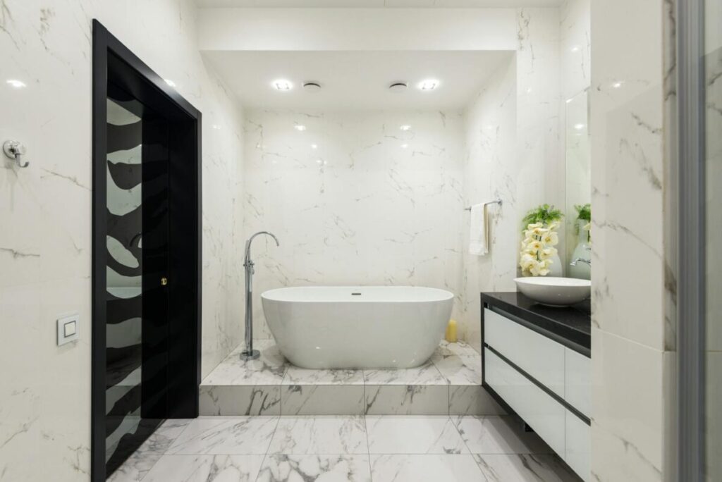 Interior of contemporary bathroom with light tiled walls and white ceramic bathtub in luxury apartment in daytime